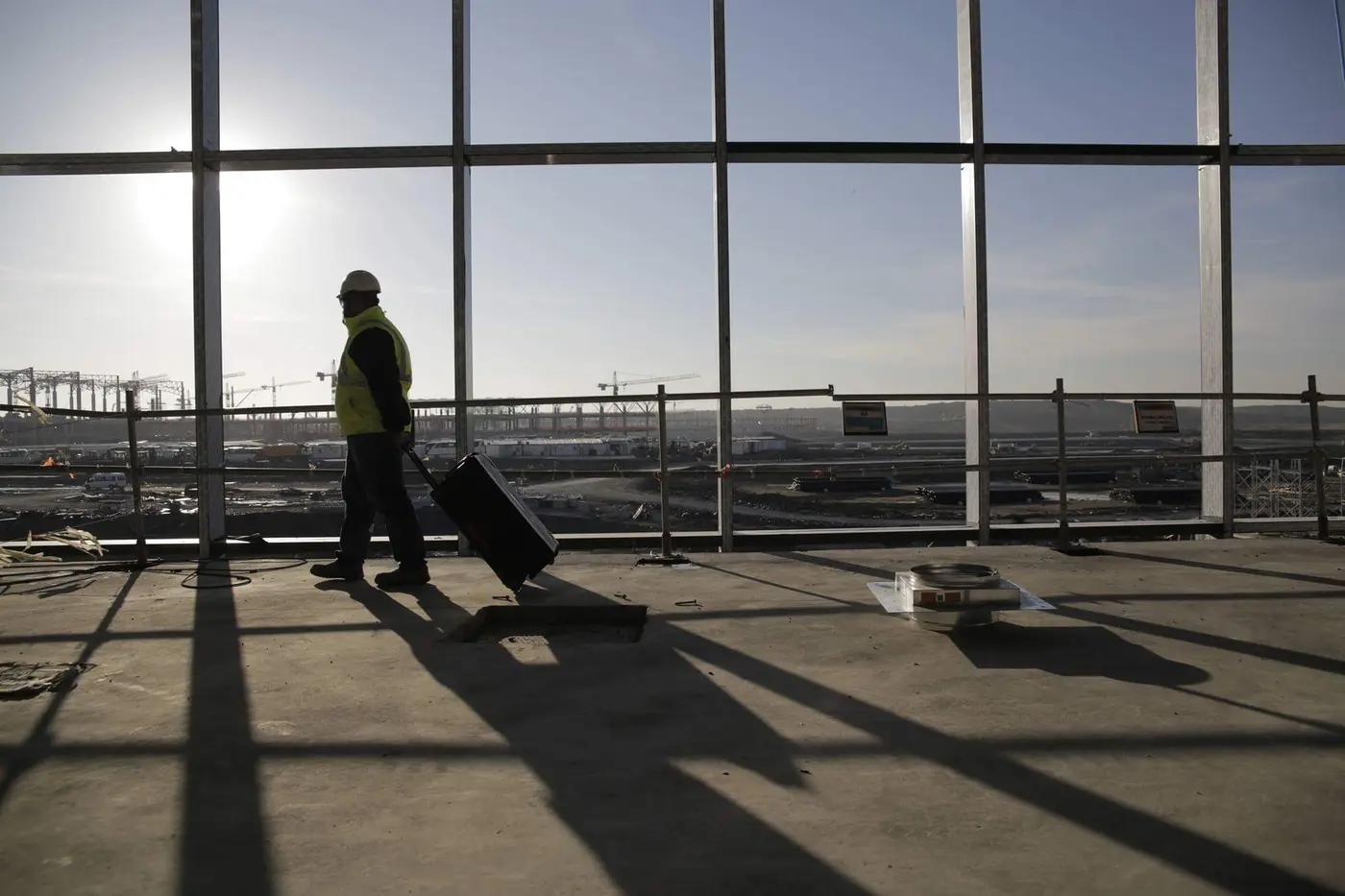 Terminal içinde cam cephe önünde ekipman taşıyan saha çalışanı